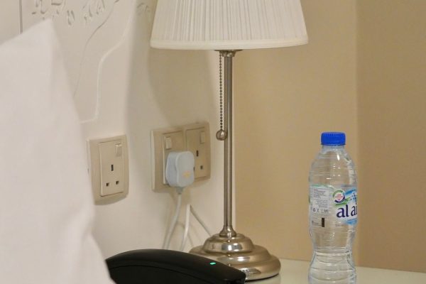 A Night Lamp Next to Bed with Water Bottle on The Nightstand